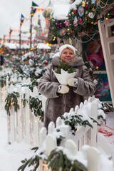 an adult woman in a fur coat on a festive square with a bouquet of Christmas trees. Christmas and New Year celebrations