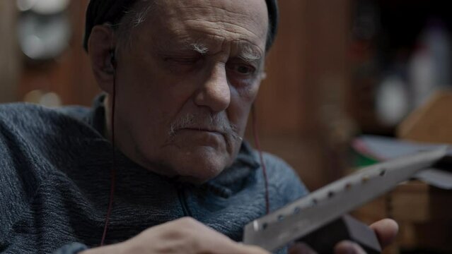 Senior gray haired male master in a wheelchair working at his workshop sharpening Japanese kitchen knife
