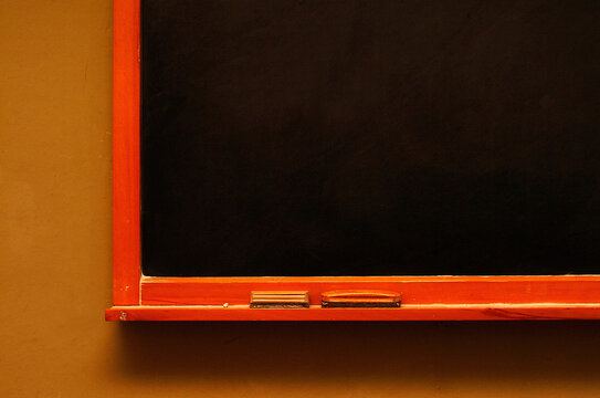 A minimalist view of a dark blackboard with a bright orange frame and a small ledge for chalk, ready for writing