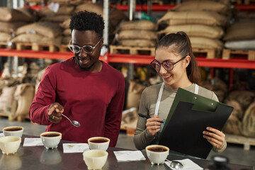 Portrait of two smiling young people discussing coffee varieties during cupping process in small coffee factory workshop