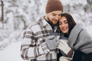 Happy beautiful couple resting and drinking hot tea in the forest in winter in the mountains