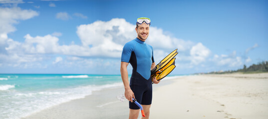 Young man with snorkeling equipment standing on a beach - obrazy, fototapety, plakaty