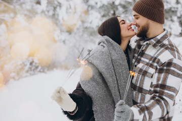 Happy romantic couple in love holding sparklers in snowy winter forest