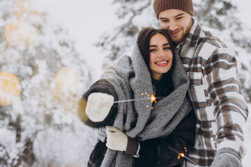 Happy romantic couple in love holding sparklers in snowy winter forest - Powered by Adobe