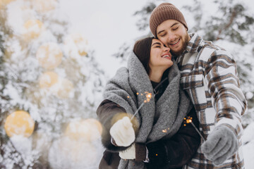 Happy romantic couple in love holding sparklers in snowy winter forest - obrazy, fototapety, plakaty