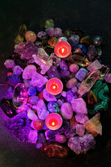 colorful crystal gemstones and burn candles in Multi colored RGB light, abstract dark background....