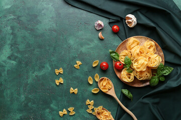 Plate and spoon with different uncooked pasta, spices and tomatoes on green background