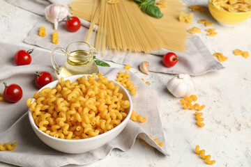 Bowl with uncooked elbow pasta, tomatoes and spices on light background, closeup