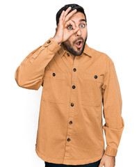 Young hispanic man wearing casual clothes doing ok gesture shocked with surprised face, eye looking through fingers. unbelieving expression.