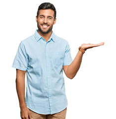 Handsome hispanic man wearing casual clothes smiling cheerful presenting and pointing with palm of...
