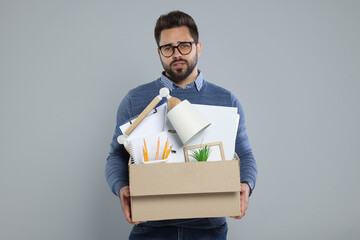Unemployed man with box of personal office belongings on light grey background