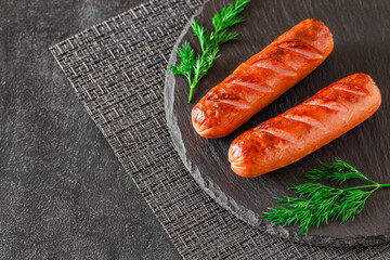Grilled sausages with herbs, incisions, on slate stone plate round, dark background, selective focus
