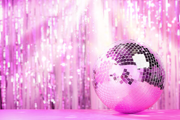 Fototapeta na wymiar Shiny disco ball on table against foil party curtain, space for text. Bokeh effect