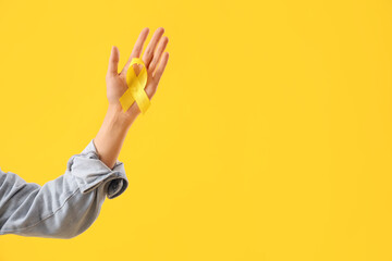 Woman with yellow awareness ribbon on color background, closeup