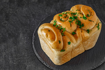 Bread with garlic and green herbs on slate stone plate round, dark background, selective focus