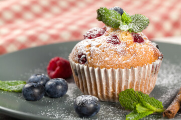 Freshly baked muffins with powdered sugar and fresh berries. Homemade muffins with fresh blueberries and raspberries on a gray plate. Homemade baking concept. Soft focus