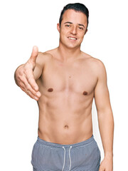 Fototapeta premium Handsome young man wearing swimwear shirtless smiling friendly offering handshake as greeting and welcoming. successful business.