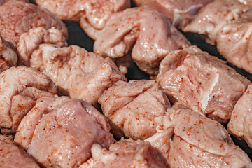 Raw red meat with spices strung on skewers in chunks is fried on coals, close-up, selective focus