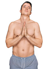 Handsome young man wearing swimwear shirtless begging and praying with hands together with hope expression on face very emotional and worried. begging.