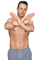 Fototapeta premium Handsome young man wearing swimwear shirtless rejection expression crossing arms and palms doing negative sign, angry face