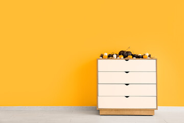 Chest of drawers with pumpkins and candles near yellow wall