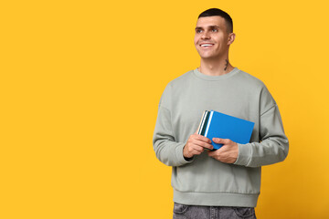 Handsome young man with books on yellow background