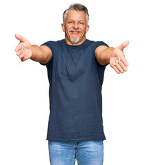 Middle age grey-haired man wearing casual clothes looking at the camera smiling with open arms for hug. cheerful expression embracing happiness.