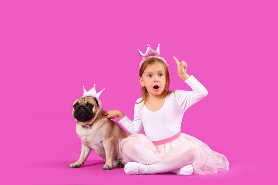 Little girl with cute pug dog in crowns pointing at something on purple background