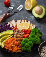 A plate with healthy vegetable salad of chicken, avocado, buckwheat, carrots, cherry tomatoes, cabbage on a dark background. Healthy lifestyle concept, complete bowl of food..
