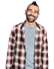 Hispanic man with ponytail wearing casual shirt looking positive and happy standing and smiling...