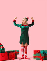 Beautiful young woman dressed as elf with Christmas gifts on pink background