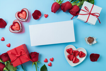 Valentine's day greeting card mock up with heart shape chocolate, gift box and  rose flowers on blue background. Top view. Flat lay
