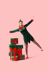 Fototapeta na wymiar Happy young woman dressed as elf with Christmas gifts on pink background