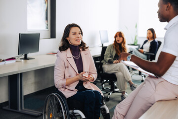 A businesswoman who uses a wheelchair is talking to multicultural colleague.