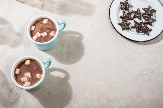 Hot cocoa in light blue and white enamel mugs with marshmallows and cookies
