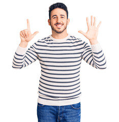 Naklejka premium Young hispanic man wearing casual clothes showing and pointing up with fingers number seven while smiling confident and happy.
