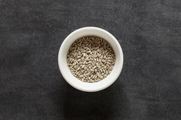 Sunflower seeds peeled kernels in white bowl, on dark background, top view, full depth of field