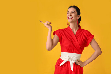 Beautiful young happy woman pointing at something on yellow background. Chinese New Year celebration