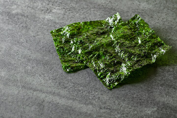 two nori sheets of dried green algae, on slate stone plate round, dark background, selective focus.