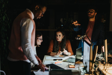 A diverse group of businesspeople collaborating in a creative office at night, analyzing reports and discussing strategies for business growth and profitability.