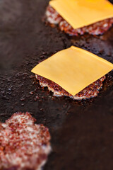 Beef patty chop covered with square piece of cheese fried on baking sheet, close-up, selective focus