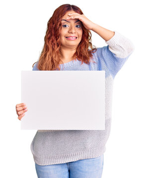 Young latin woman holding blank empty banner stressed and frustrated with hand on head, surprised and angry face