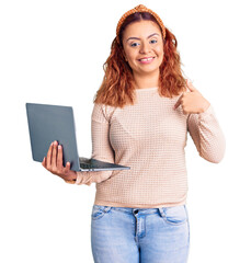 Young latin woman holding laptop pointing finger to one self smiling happy and proud