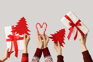 Hands holding Christmas gifts, candy canes and paper fir trees on grey background