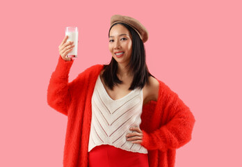 Young Asian woman with glass of milk on pink background
