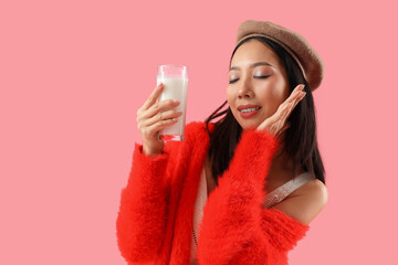 Young Asian woman with glass of milk on pink background