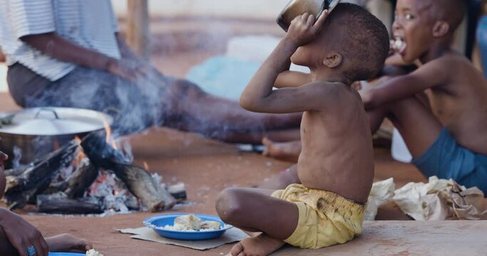 Poor, malnourished Black African child due to extreme poverty, drought and climate change. Drinking water from a cooking pot
