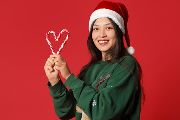 Young Asian woman in Santa hat with candy canes on red background