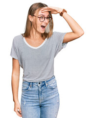 Beautiful young blonde woman wearing casual clothes and glasses very happy and smiling looking far away with hand over head. searching concept.