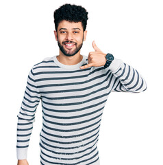 Fototapeta premium Young arab man with beard wearing casual striped sweater smiling doing phone gesture with hand and fingers like talking on the telephone. communicating concepts.